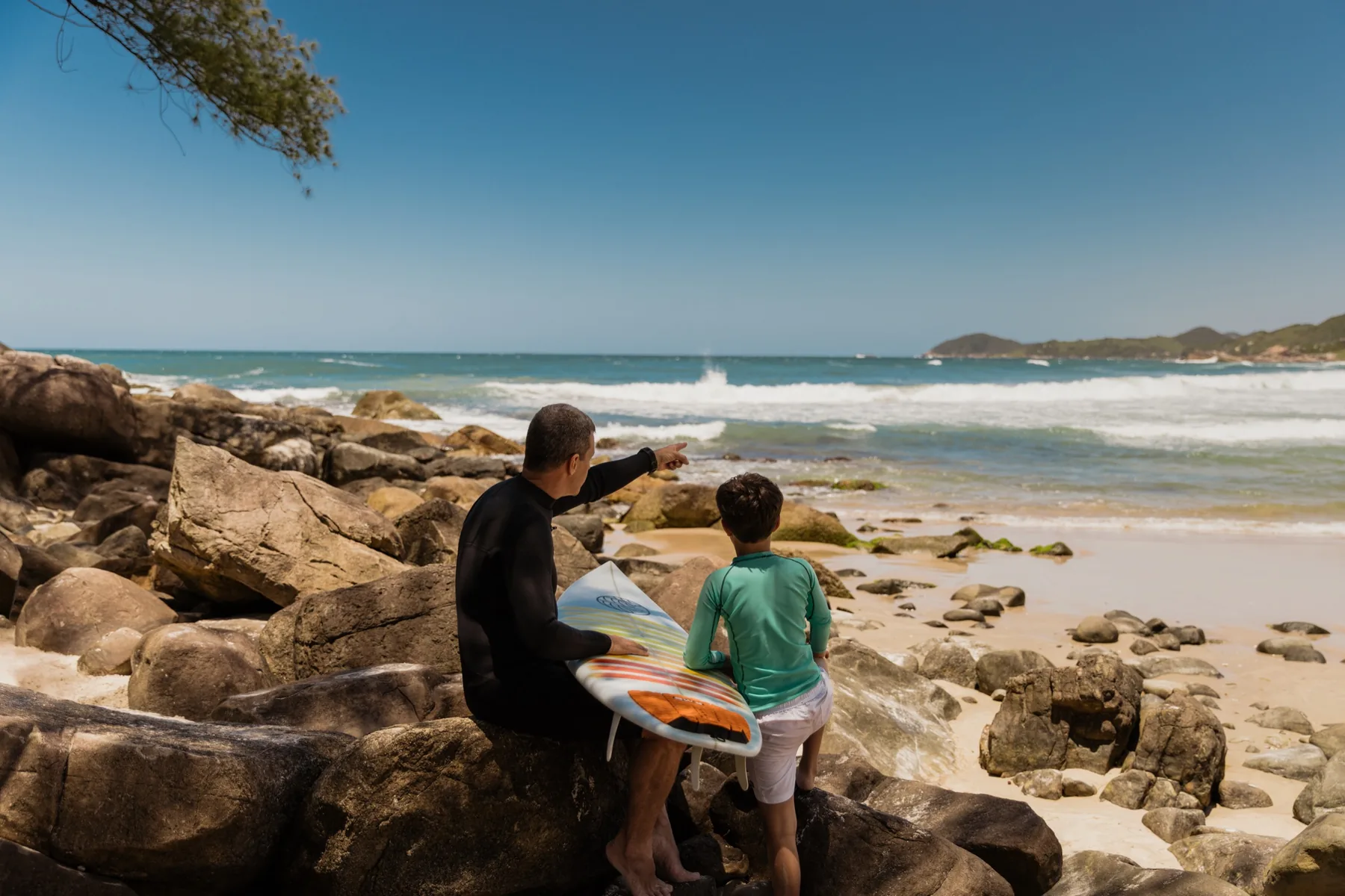 Pai e filho contemplando o mar com uma prancha